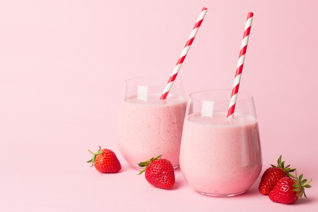 A glass of fresh strawberry smoothie on a pink background