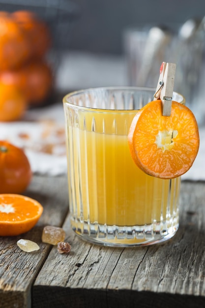 Glass of fresh tangerine juice with ripe tangerines on old wooden table, rustic style