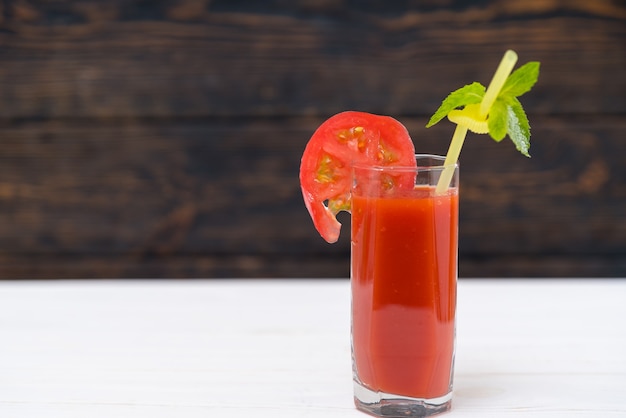 Стакан свежего овощного сока с ломтиком помидора и листом мяты на пластиковой соломке