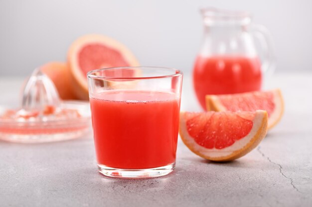 A glass of freshly made grapefruit juice and slices of fresh fruit on a light concrete background