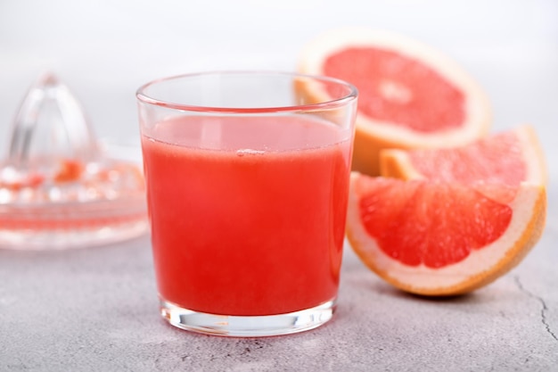 A glass of freshly made grapefruit juice and slices of fresh fruit on a light concrete background