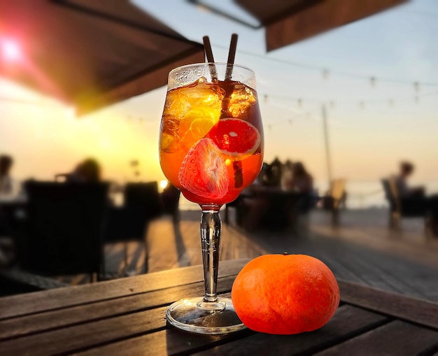 glass of fruit water   and mandarin on wooden  table on beach cafe at sunset on sea