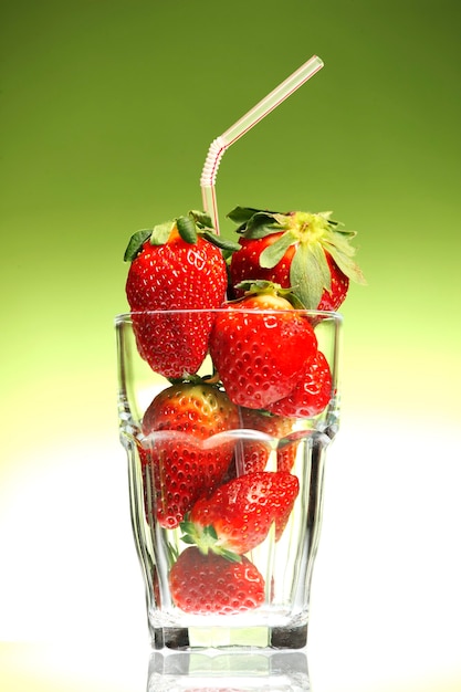 a glass full of strawberries against green background