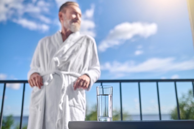 Glass full of water placed on the table beside a vacationer leaning on the railing