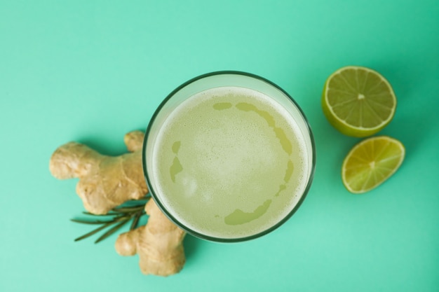 Glass of ginger beer and ingredients on mint background