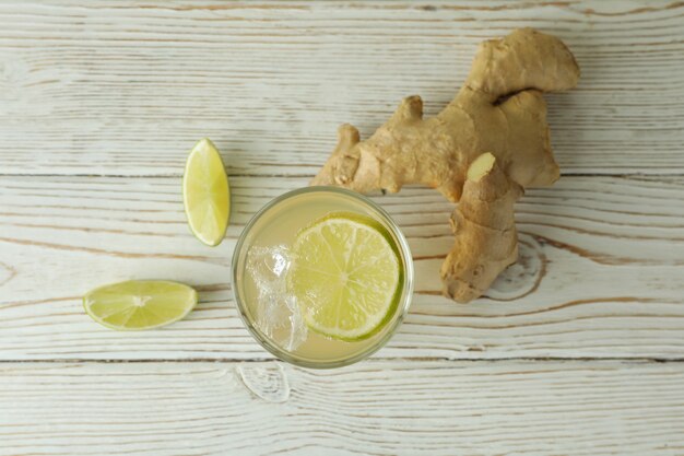 Glass of ginger beer and ingredients on white wooden table