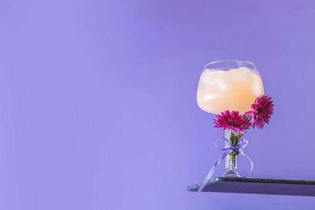 Glass of gintonic with slices of grapefruit decorated fresh chrysanthemums on bright violet background Spring summer art drink food concept