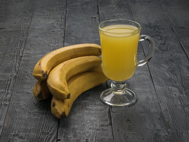 Un bicchiere di vetro su uno stelo con frullati e banane su uno sfondo rustico piatto lay