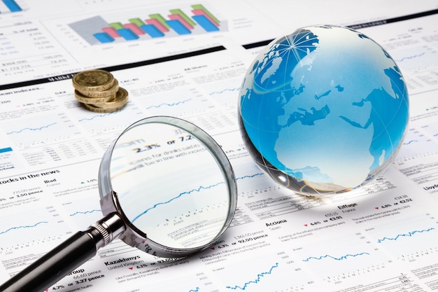 Glass Globe, Magnifying Glass And Coins On Financial Reports Close-up