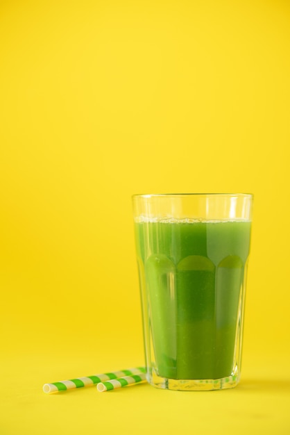 Glass of green celery smoothie on yellow background