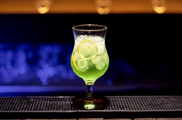 A glass of green cocktail stands at the bar in a nightclub