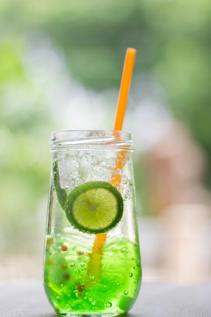 A glass of green cocktail with a straw in it and a straw in the background.