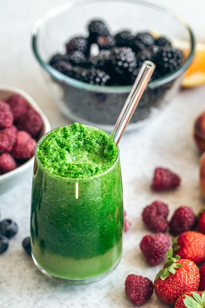 Glass of green smoothie on blurred kitchen table with berries