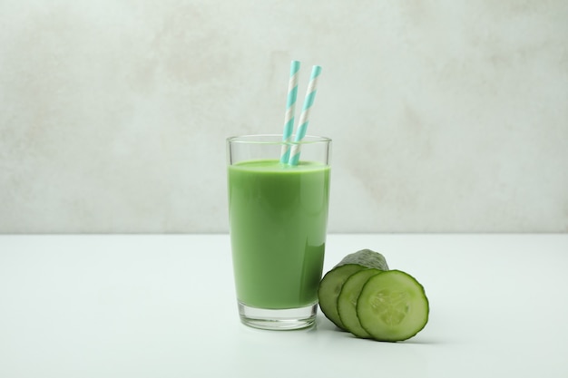 Glass of green smoothie and cucumber on white table