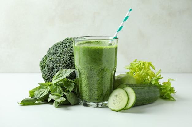 Glass of green smoothie and ingredients on white table