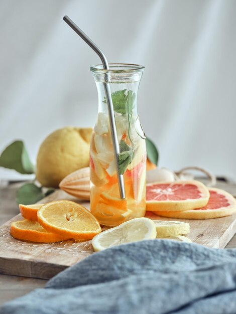 Glass of healthy lemonade with lemon orange and mint leaves and sliced fruits on wooden chopping board
