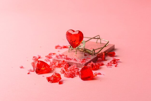 Стеклянное сердце в мышеловке на розовом фоне. Креативная концепция ко Дню святого Валентина.