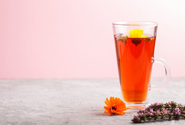 Glass of herbal tea with calendula and hyssop on gray and pink