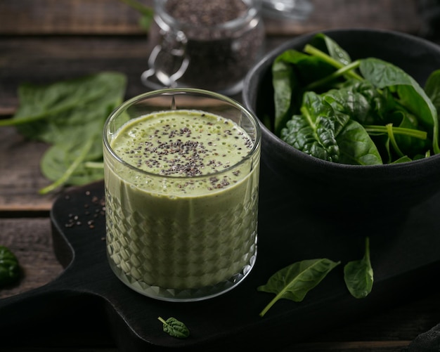 Glass of homemade healthy green smoothie with fresh baby spinach and chia seeds on dark wooden background. Food and drink, dieting and healthy eating concept