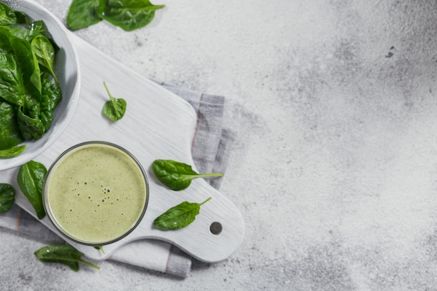 Glass of homemade healthy green smoothie with fresh baby spinach on light background. Food and drink, dieting and healthy eating concept