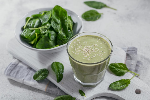 Glass of homemade healthy green smoothie with fresh baby spinach and sesame seeds on light background Food and drink dieting and healthy eating concept