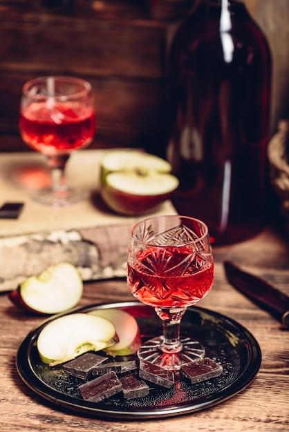 Photo glass of homemade redcurrant nalivka with apple slices and chocolate