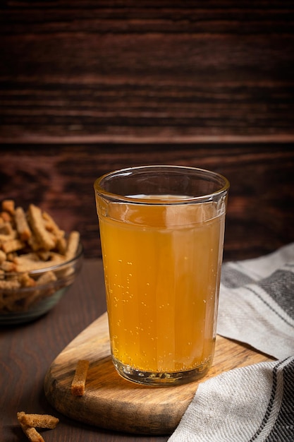 Glass of homemade traditional fermented kvass served with salted dry roast snack on wooden table