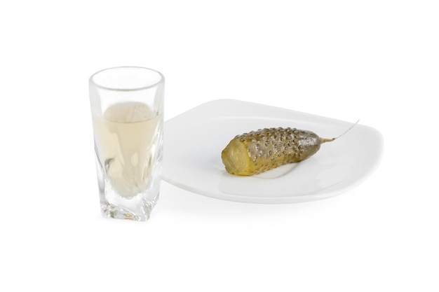 glass of homemade vodka and bitten salted cucumber on a plate isolated on white background