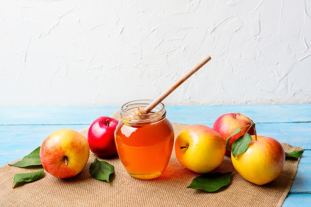 Glass honey jar with dipper and apples copy space