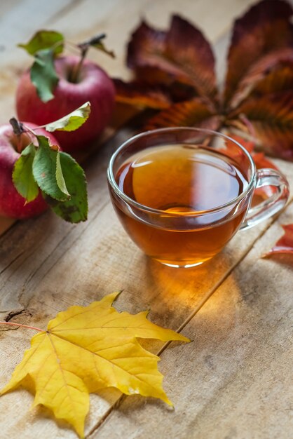 Glass hot cup of tea on a wooden table with autumn leaves and apple