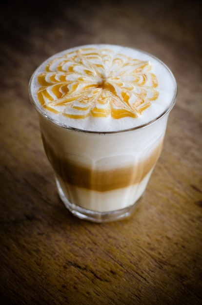 a glass of hot latte art coffee on wooden table