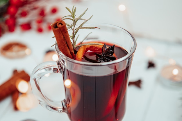 Glass of hot mulled wine with rosemary on a white plate close-up.