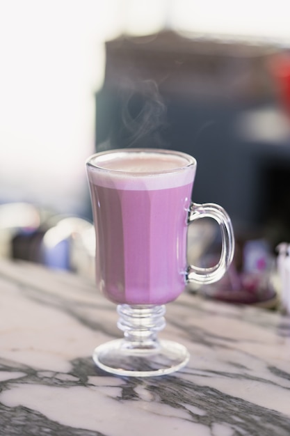 A Glass of hot taro cappuccino coffee in a cafe shop.