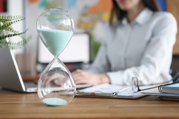 Photo glass hourglass standing against background of woman working at laptop closeup