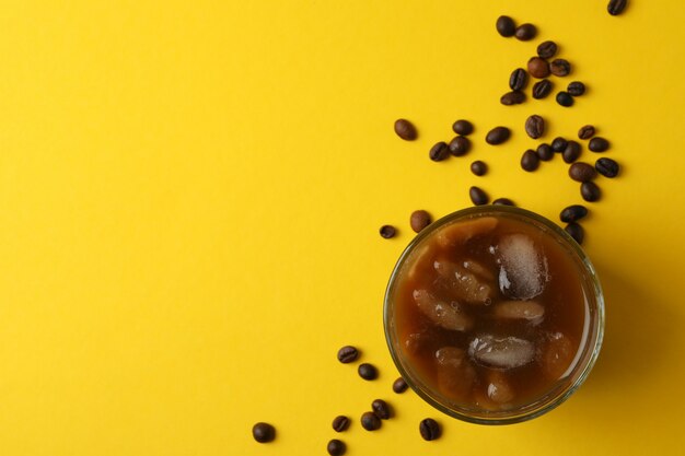 Glass of ice coffee on yellow background. Fresh drink