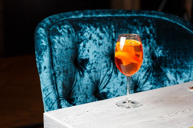 Стакан ледяного коктейля Aperol spritz подается в бокале, украшенном ломтиками апельсина на черном фоне