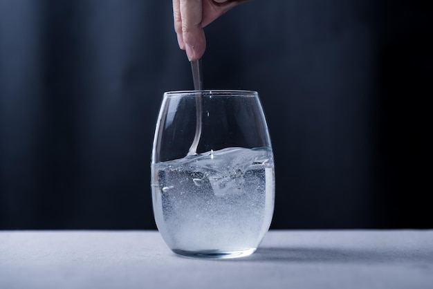 A glass of ice water with a spoon being dipped into it.