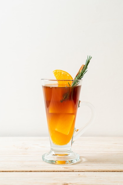 A glass of iced americano black coffee and layer of orange and lemon juice decorated with rosemary and cinnamon on wood table