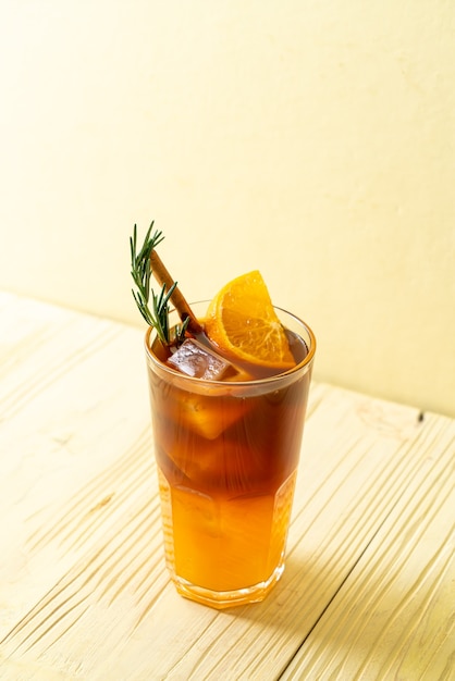 A glass of iced americano black coffee and layer of orange and lemon juice decorated with rosemary and cinnamon