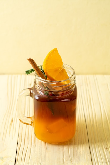 A glass of iced americano black coffee and layer of orange and lemon juice decorated with rosemary and cinnamon