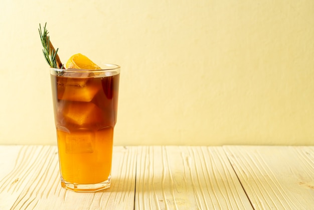 アイスアメリカーノブラックコーヒーのグラスとローズマリーとシナモンで飾られたオレンジとレモンジュースの層