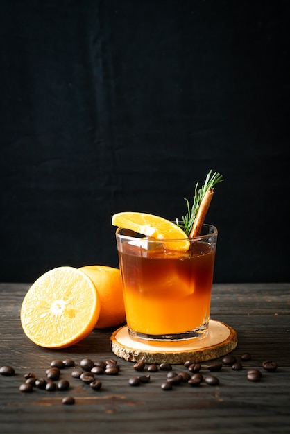 A glass of iced americano black coffee and layer of orange and lemon juice decorated with rosemary and cinnamon