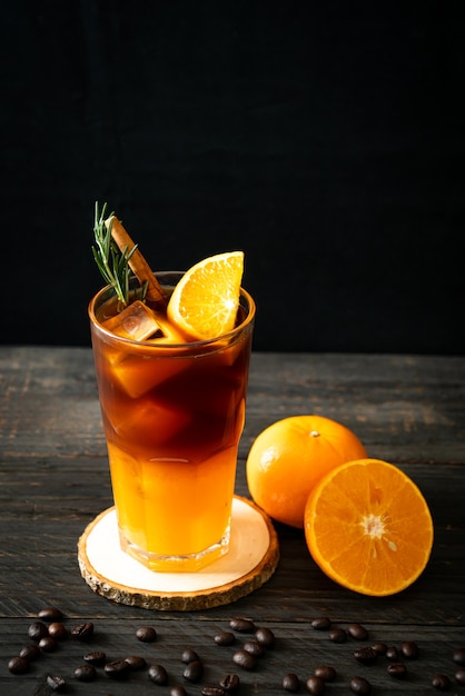 A glass of iced americano black coffee and layer of orange and lemon juice decorated with rosemary and cinnamon