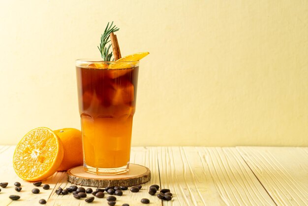 A glass of iced americano black coffee and layer of orange and lemon juice decorated with rosemary and cinnamon