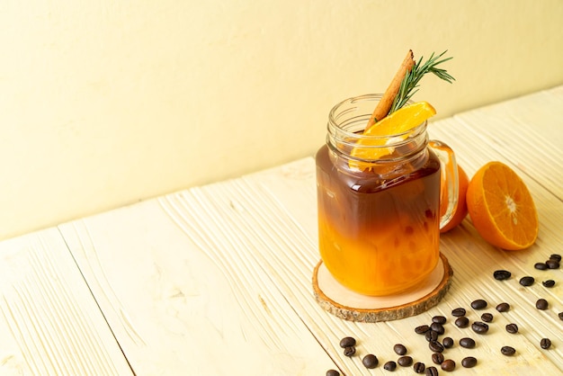 A glass of iced americano black coffee and layer of orange and lemon juice decorated with rosemary and cinnamon