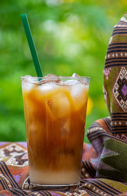 緑のストローが付いたアイスコーヒーのグラスが、ティーポットとティーポットを背景にしたテーブルの上に置かれています。