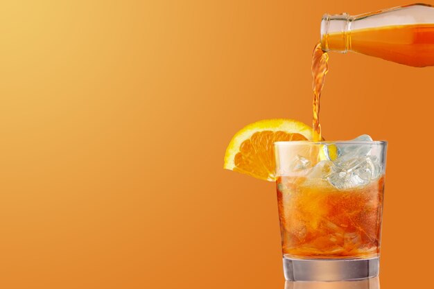 오렌지 조각으로 장식 된 아이스 콜드 분출 칵테일 잔. 아페리티프, coctail 만들기, 오렌지 배경에 고립 된 얼음이 가득한 유리에 액체를 붓는. 공간 복사