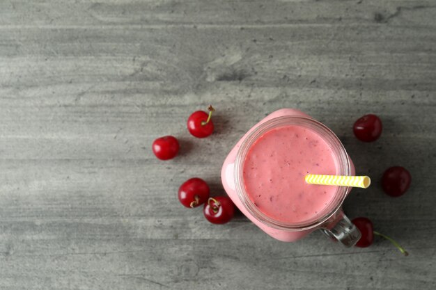 Glass jar of cherry smoothie and ingredients on gray textured table