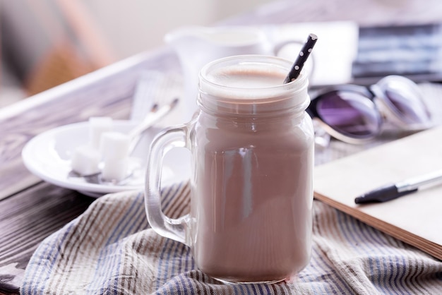 Glass jar of coffee with cream Tablet Sunglasses and sugar on background Wooden table