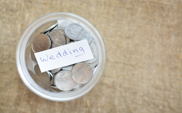 Glass jar filled with coins labeled with the words wedding view from above background of burlap the concept of saving money accumulating finances
